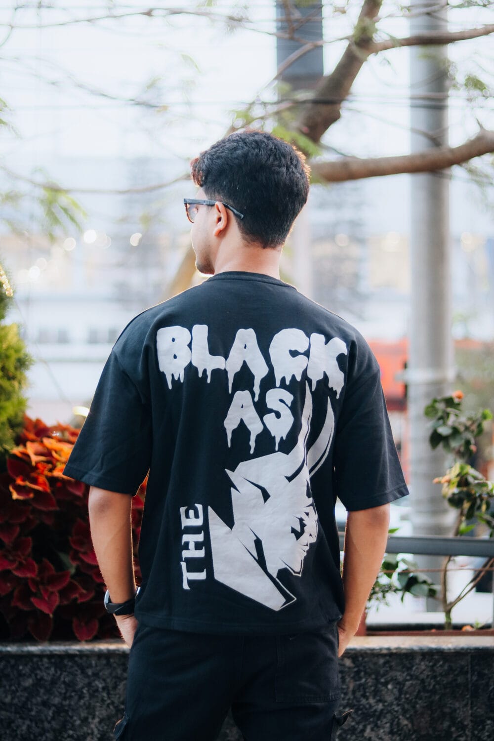 A man wearing a LUCIFER : BLACK AS THE DEVIL Oversized T-Shirt back view.