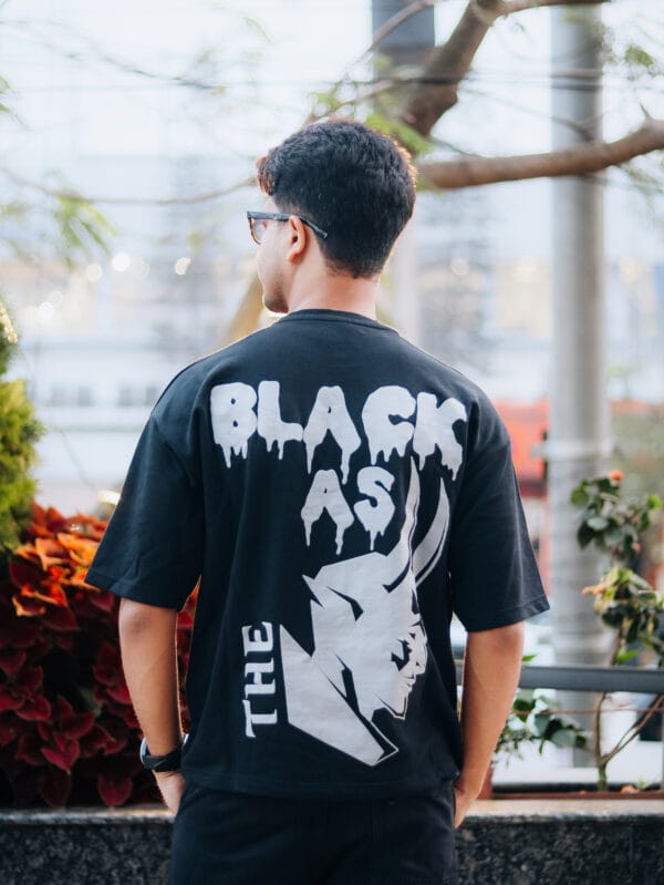 A man wearing a LUCIFER : BLACK AS THE DEVIL Oversized T-Shirt back view.